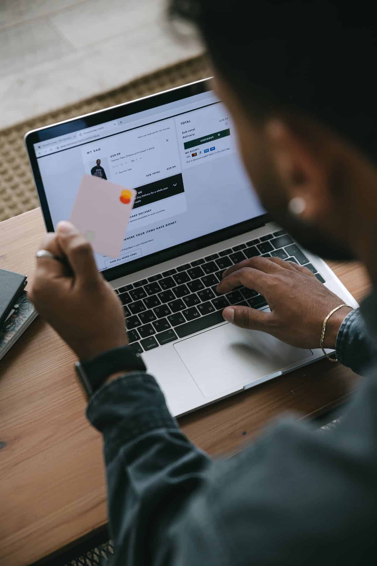 شخص يحمل بطاقة دفع أمام حاسوب محمول ليتم عملية شراء عبر الإنترنت